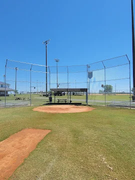Green chain-link and netted batting cage enclosure around a baseball practice mound and home plate on grass field