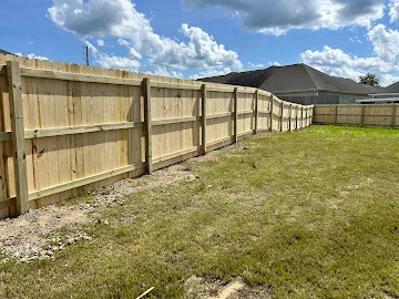 New wood privacy fence with vertical pickets and wood posts along a grassy backyard lawn