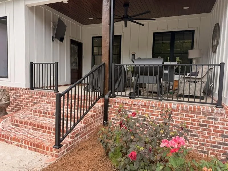 Black aluminum railing with vertical balusters on red brick porch steps and covered front porch