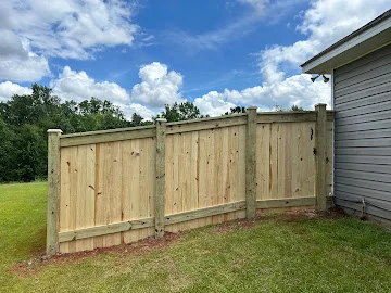 New wood privacy fence with vertical pickets and capped posts beside a gray vinyl-sided house on a grassy lawn