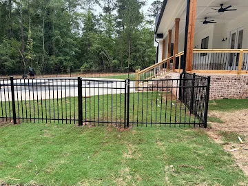 Black aluminum picket pool fence with gate installed on sloped lawn beside brick porch foundation