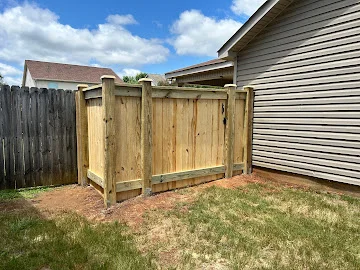 New pressure-treated wood privacy fence with vertical pickets and cap rail beside vinyl-sided house, next to weathered wood fence