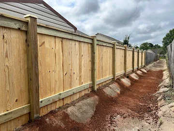Wood privacy fence with vertical pickets, horizontal rails, and wood posts installed over red clay soil with base rocks