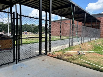 Black vinyl-coated chain link fence with swing gate along concrete walkway under metal canopy