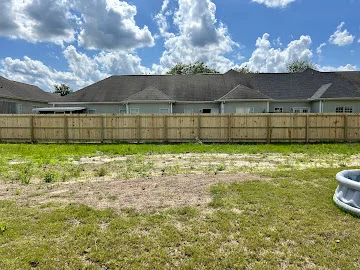 Natural wood privacy fence with horizontal boards and vertical posts along a grassy backyard lawn