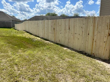 Tall natural wood privacy fence with vertical pickets running along a grassy backyard property line