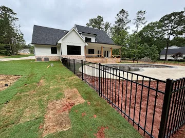 Black aluminum picket fence enclosing an in-ground pool beside a new white home with covered porch