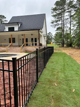 Black aluminum picket fence installed alongside new sod and a pool area beside a newly built home with a covered porch