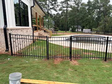 Black aluminum picket pool fence installed along brick house with new sod and concrete pool deck