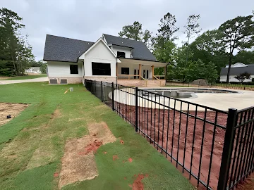 Black aluminum picket pool fence installed around an in-ground pool with new sod and red clay soil