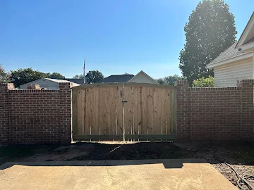 Wood privacy gate with vertical boards set between red brick wall sections over a concrete walkway