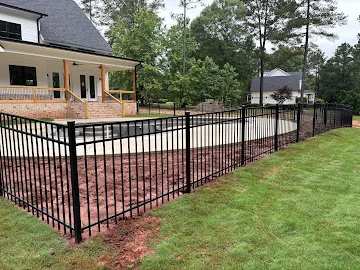 Black aluminum picket fence with horizontal rails installed along a curved residential yard edge near a brick front porch
