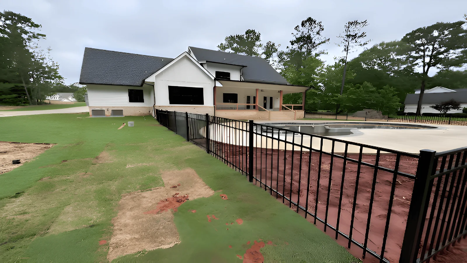 Black aluminum pool fence with vertical pickets beside a concrete pool deck and newly sodded lawn