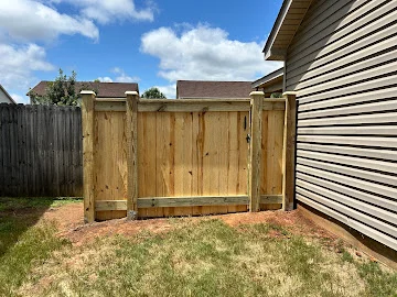 Pressure-treated wood privacy fence with vertical pickets, wood posts, and a gate section beside vinyl siding house