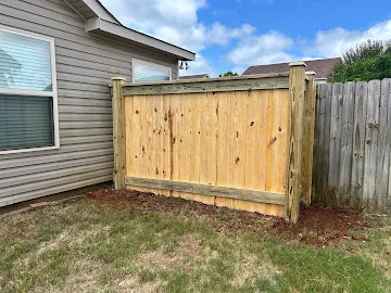 New pressure-treated pine privacy fence with vertical boards and horizontal rails beside a vinyl-sided house