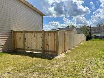 Wood privacy fence with framed gate and vertical pickets along a grassy side yard beside a vinyl-sided house