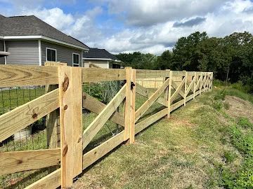 Pressure-treated wood rail fence with diagonal braces and wire mesh panels along a grassy slope