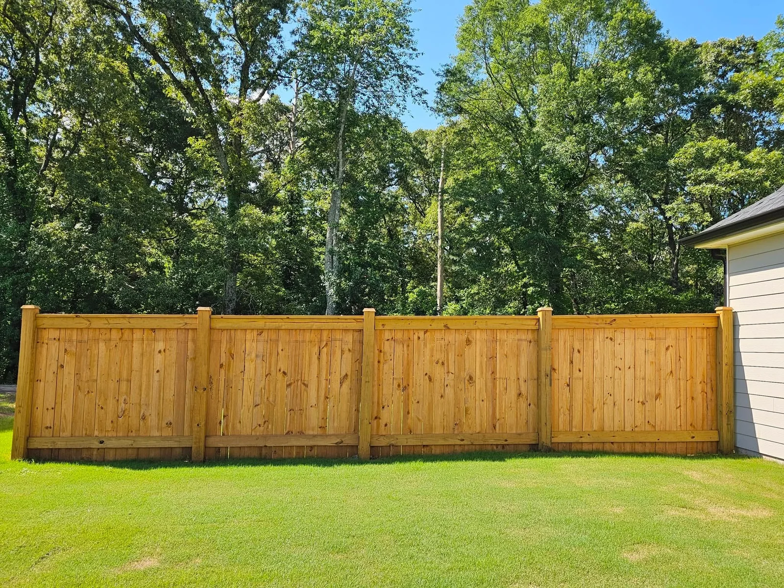 A freshly installed wood privacy fence running along the backyard of a residential home in Warner Robins, Georgia, with green grass and mature trees visible behind the fence line.